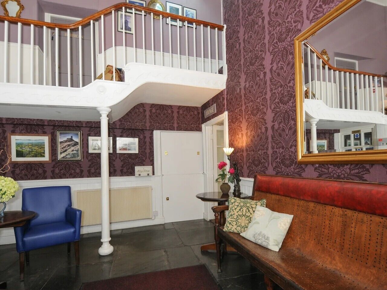 A room with a staircase, a blue chair, a red sofa, and a mirror on the wall.