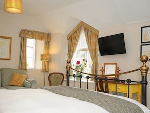 Ein Schlafzimmer mit einem Bett, einem Sessel, einem Schreibtisch, einem Fernseher und einem Fenster mit Vorhängen.