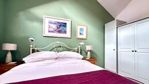 Un dormitorio con una cama, dos mesitas de noche con lámparas, un armario y dos cuadros en la pared.