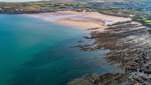An aerial view of a coastal area with a sandy beach, rocky shoreline, and a town in the background. - 4 Bed in Braunton (oc-56111) (Croyde)