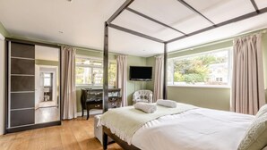 A bedroom with a four-poster bed, a desk with a chair, a TV, and a view of the outdoors. - 4 Bed in Braunton (oc-56111) (Croyde)