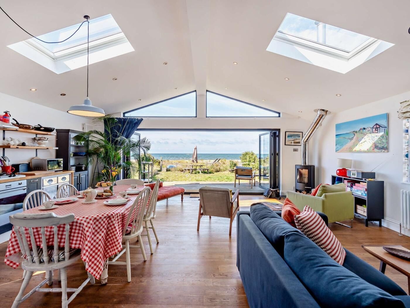 Een ruime woonkamer met een grote eettafel, een bank en uitzicht op de zee door een glazen deur.