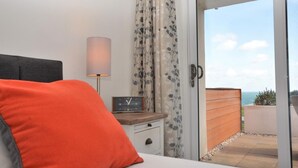 Un dormitorio con cama, mesita de noche, lámpara, reloj y vistas al exterior a través de una puerta corredera.