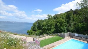 Una piscina con vista al mar, rodeada de césped y árboles.