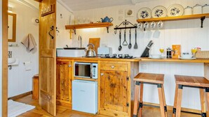 Een compacte keuken met houten kastjes, een ingebouwde magnetron, een gasfornuis en een kleine koelkast.