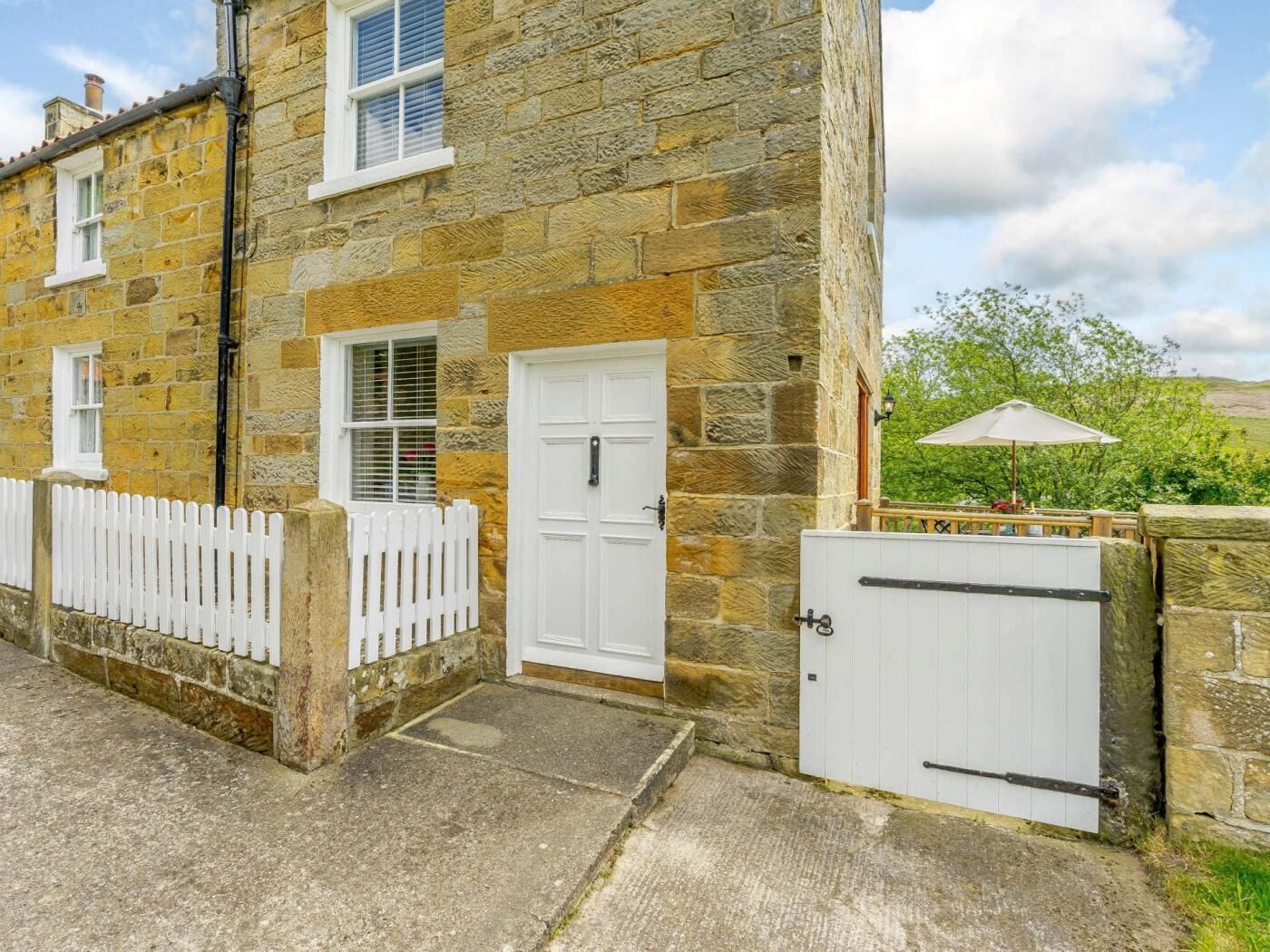 A stone building with a white door, a white picket fence, and a gated entrance.