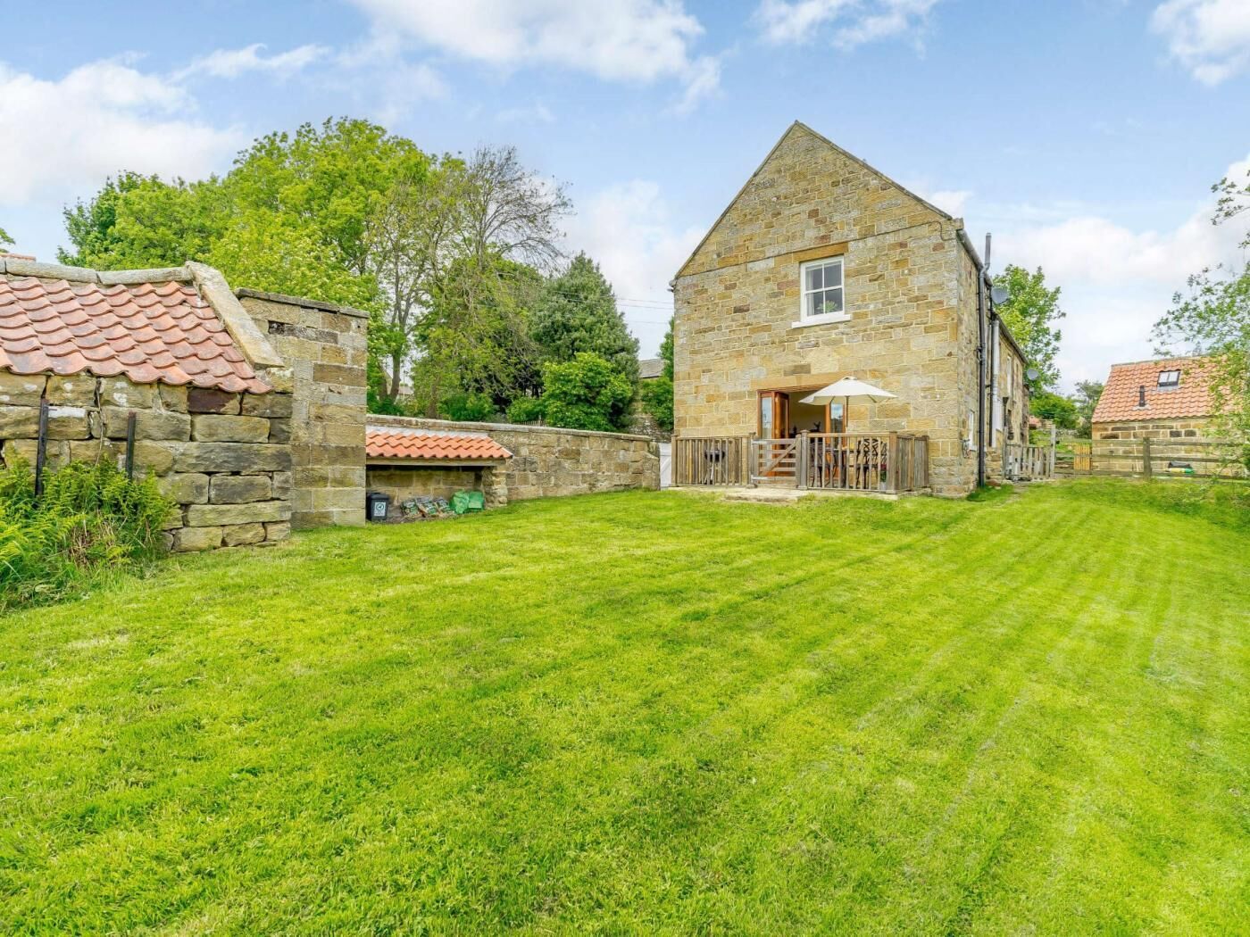A stone building with a sloped roof, a small porch with a railing, and a well-maintained lawn.