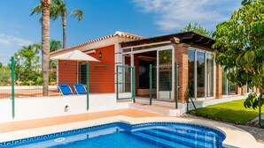 Zona de piscina amb una piscina blava cristal·lina, una zona de seients coberta amb cadires blaves i un edifici de maó amb portes de vidre.