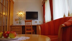A room with a television, a dining table with apples, a chair, and a sofa. - Hotel Bergland (Schenna)