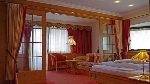 A room with a bed, a sofa, a chair, a table, and a lamp. - Hotel Bergland (Schenna)