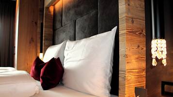 Una cama bien tendida con sábanas blancas y almohadas rojas, un cabecero oscuro y una pared de madera decorativa con una lámpara.