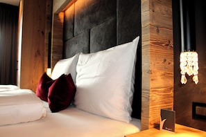 A neatly made bed with white linens and red pillows, a dark headboard, and a wooden accent wall with a light fixture.