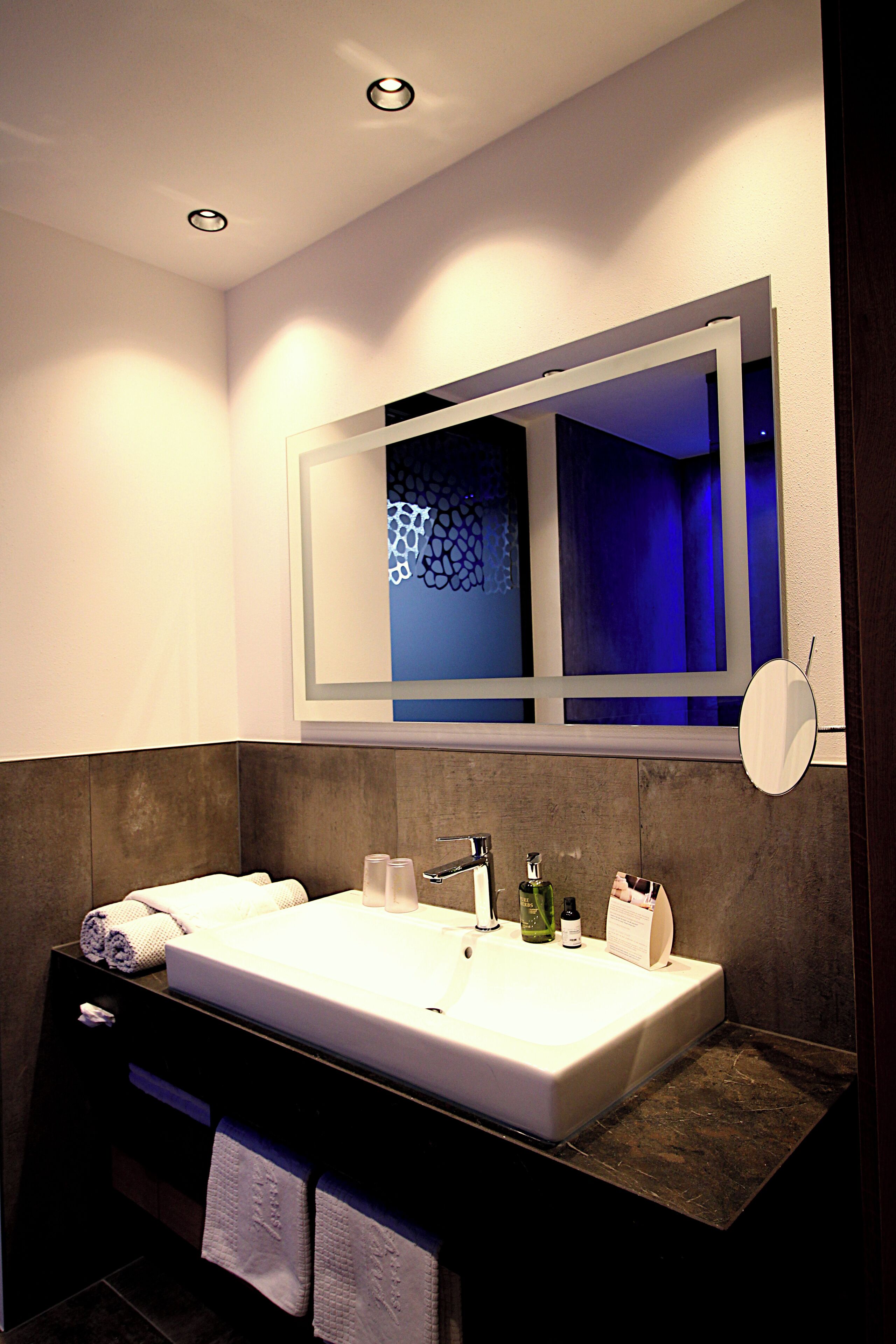 A modern bathroom with a large mirror, a white sink, and a dark countertop.