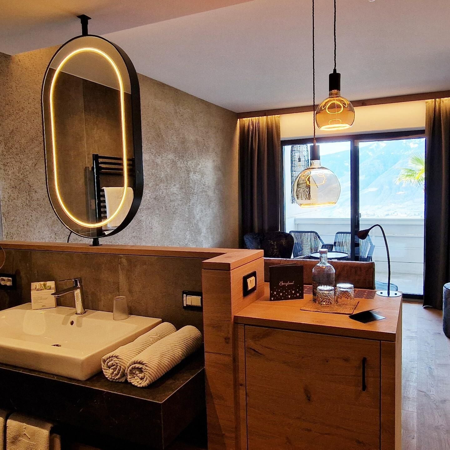 Une salle de bain moderne avec un grand miroir, une baignoire, un meuble-lavabo en bois et une vue sur l’extérieur.