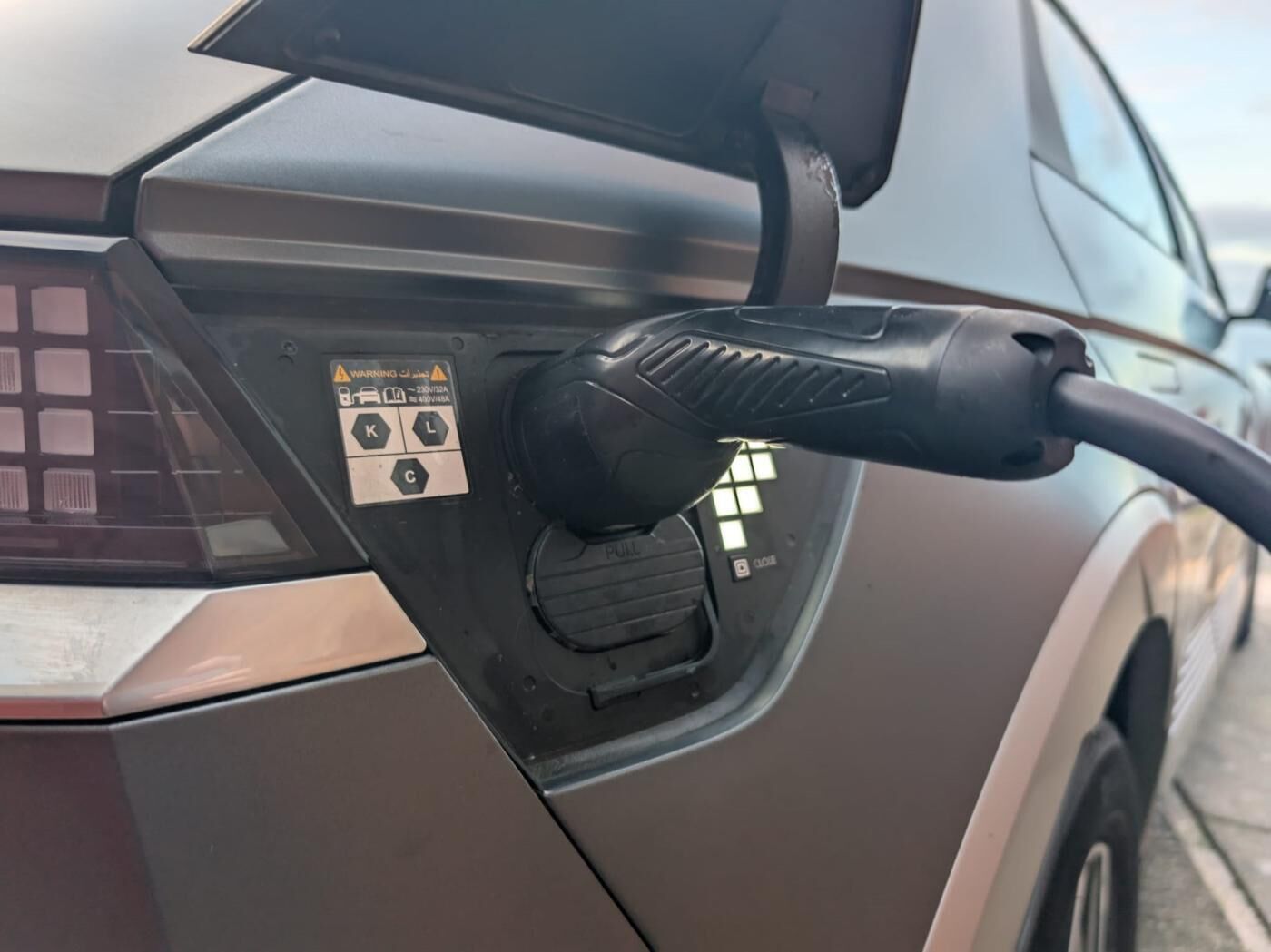 Une borne de recharge pour voitures, dotée de panneaux d’avertissement et d’une prise.