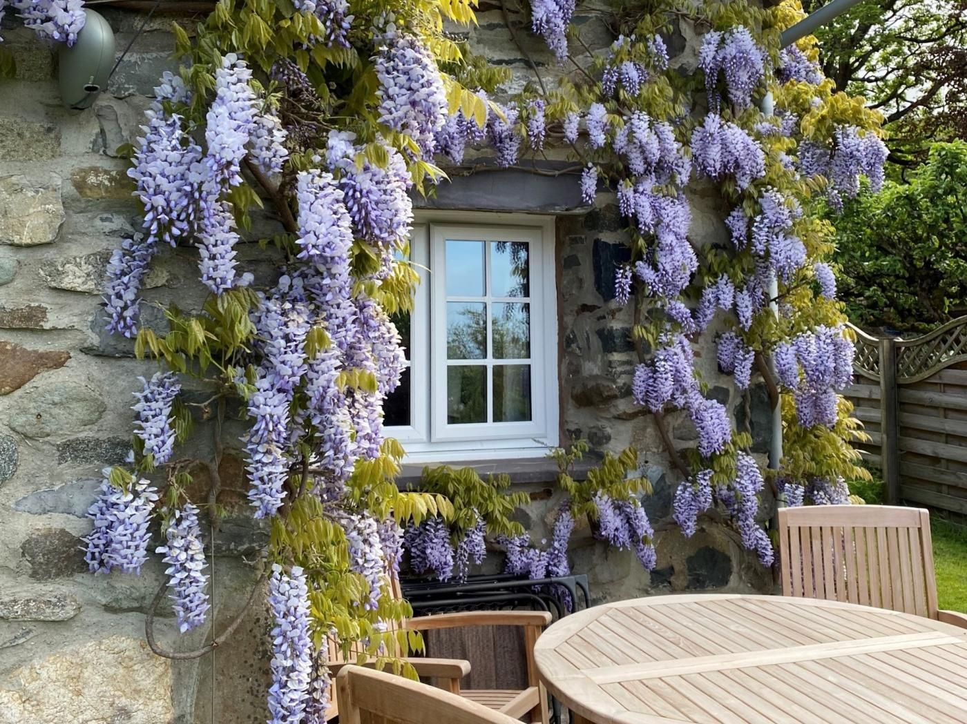 Un bâtiment en pierre avec une fenêtre, et une table et des chaises en bois devant.