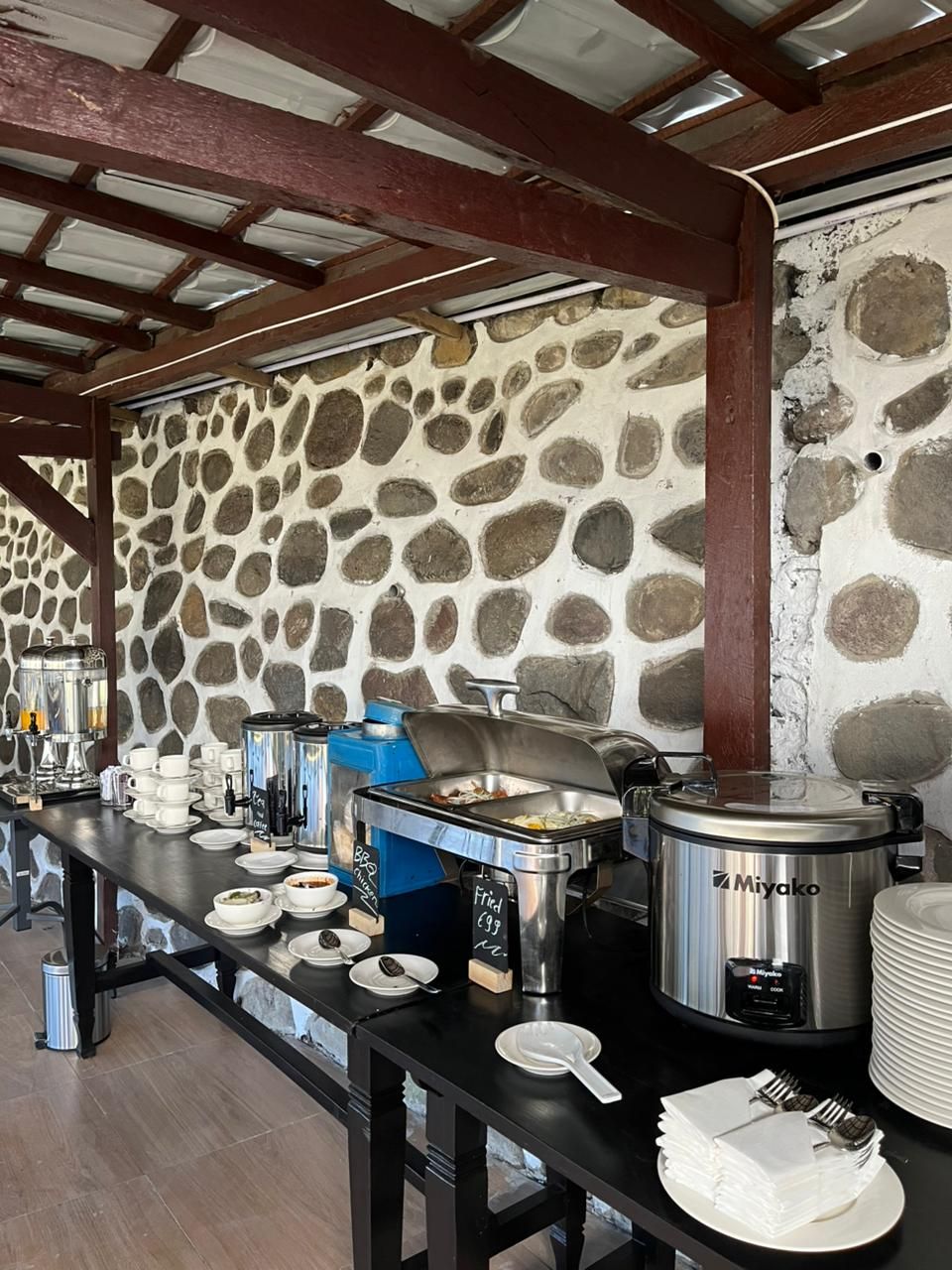 Un buffet est installé sur une table, avec différents plats et ustensiles, le tout placé devant un mur de pierres.