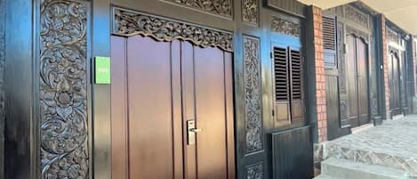 Un juego de puertas dobles de madera oscura con tallas intrincadas, un letrero verde con número y una escalera enlosada que sube a un nivel superior.