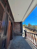 A covered outdoor area with a stone floor, a wooden door, and a metal railing.