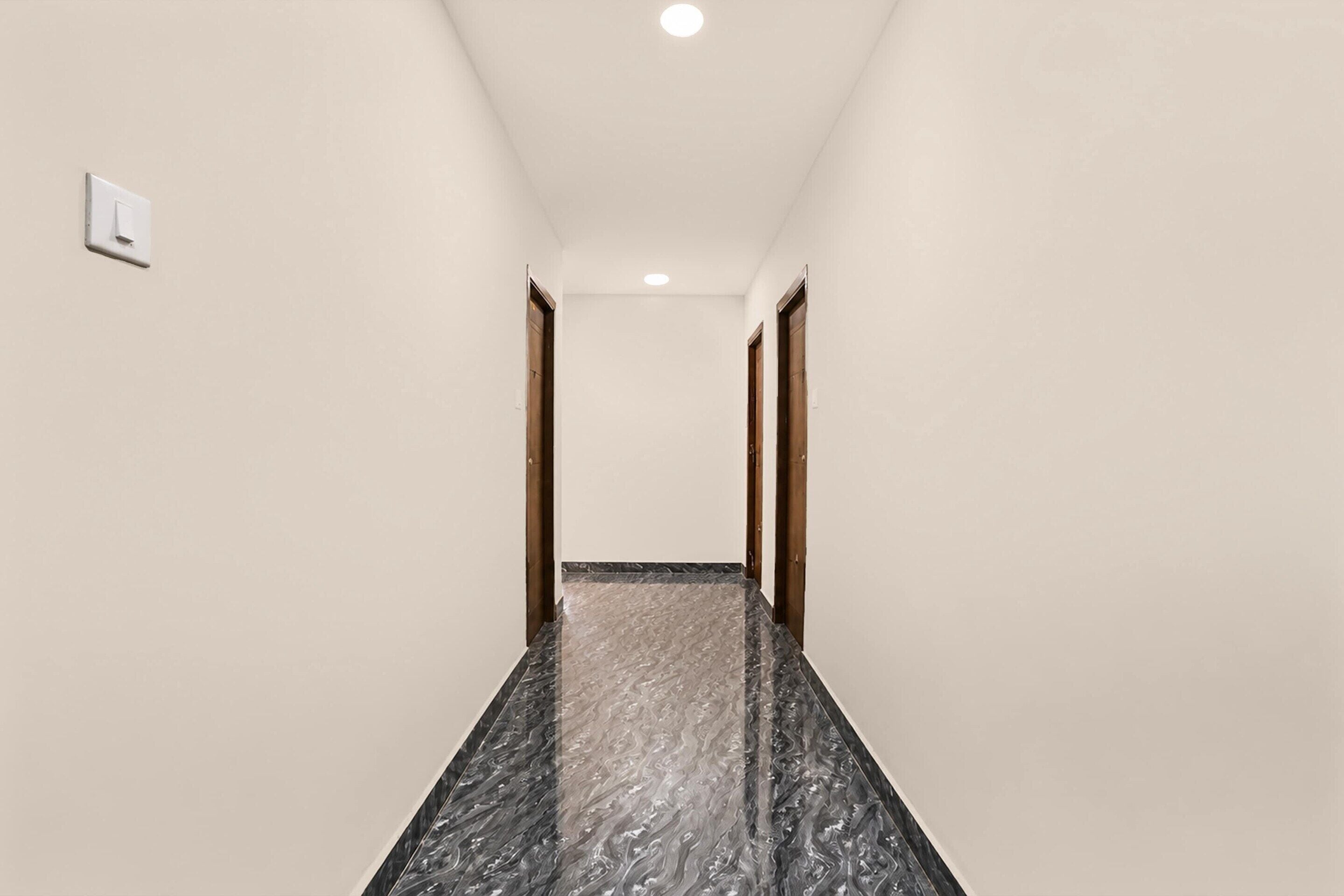 A corridor with a marble floor, wooden doors, and a light switch on the wall.