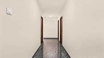A corridor with a marble floor, wooden doors, and a light switch on the wall.