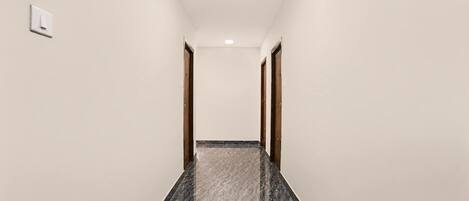 A corridor with a marble floor, wooden doors, and a light switch on the wall.