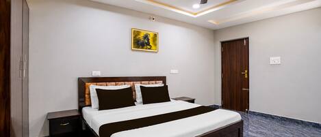 Una habitación de hotel con cama, mesitas de noche, ventilador de techo, un cuadro y una puerta.
