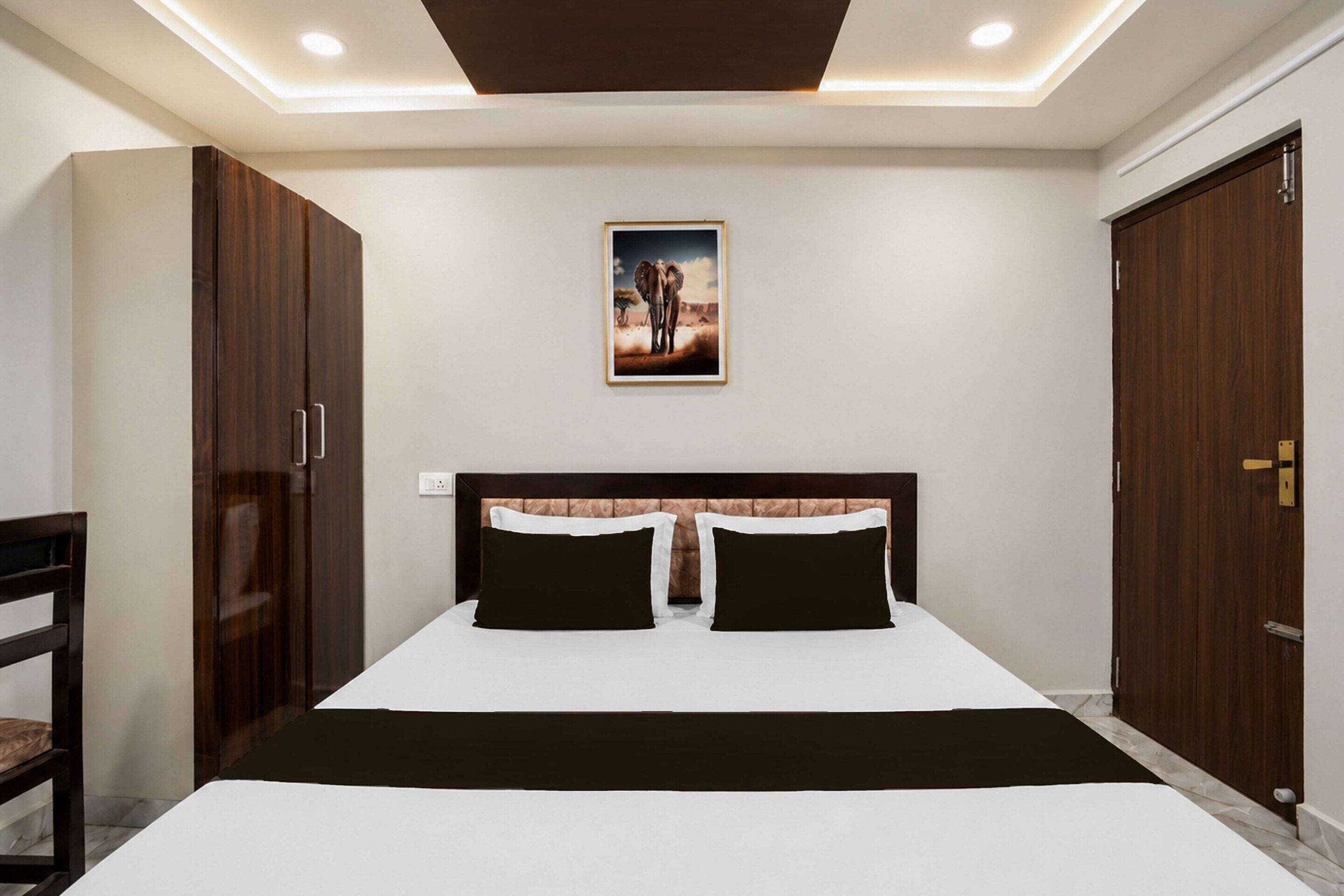 Un dormitorio con una cama grande, dos mesitas de noche, un armario de madera, un cuadro enmarcado en la pared y una lámpara en el techo.
