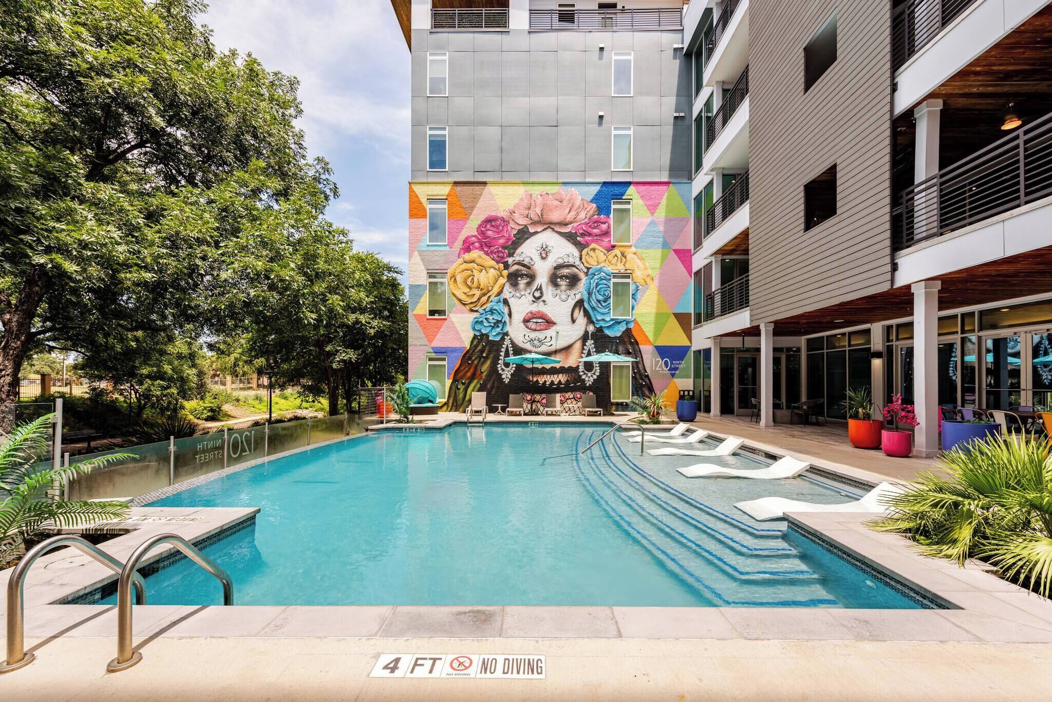 A swimming pool with a mural, a 4 ft no diving sign, and a building with balconies.