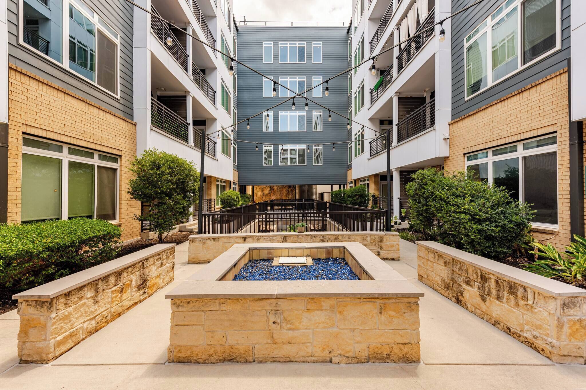 A multi-story residential building with balconies, a central courtyard with a water feature, and a stone pathway.