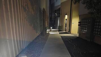 A nighttime pathway flanked by buildings, a metal fence, and a wall with circular patterns.