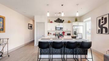 A modern kitchen with a central island, bar stools, white cabinetry, and pendant lighting.