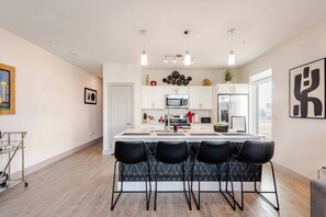 A modern kitchen with a central island, bar stools, white cabinetry, and pendant lighting. - Riverwalk Downtown Luxury Pool & Free Parking (San Antonio)
