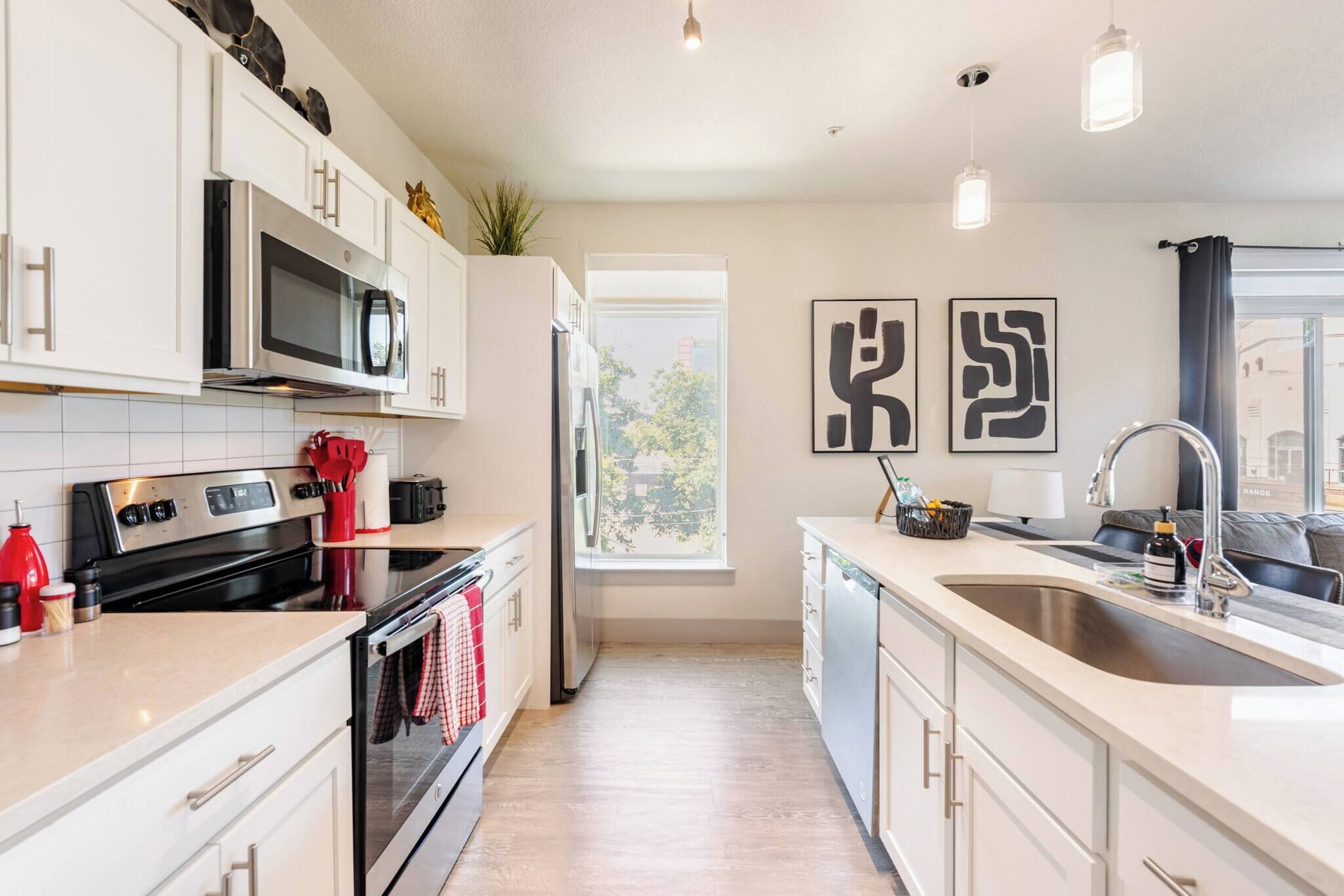 A modern kitchen with white cabinetry, stainless steel appliances, a large window, and a view of the outside.