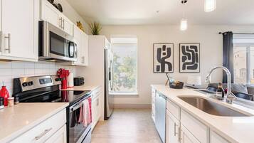 A modern kitchen with white cabinetry, stainless steel appliances, a large window, and a view of the outside.