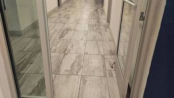 Pasillo de hotel con suelo de baldosas, puertas de vidrio y señalización de ruta de evacuación.