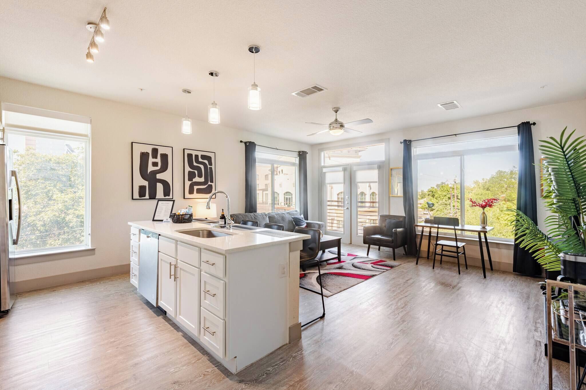 A modern kitchen with a central island, a dining area with a table and chairs, and large windows with curtains.