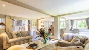 A spacious living room with a sofa, armchairs, a coffee table, and a dining area visible through an open door. - 6 Bed in Lymington (oc-56765) (Boldre)