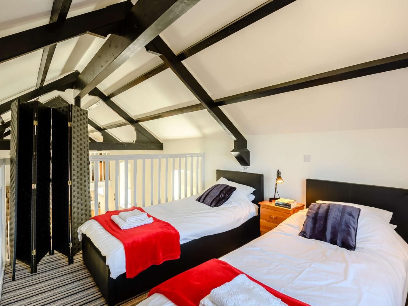 A hotel room with two beds, a wooden ceiling, and a nightstand with a lamp.
