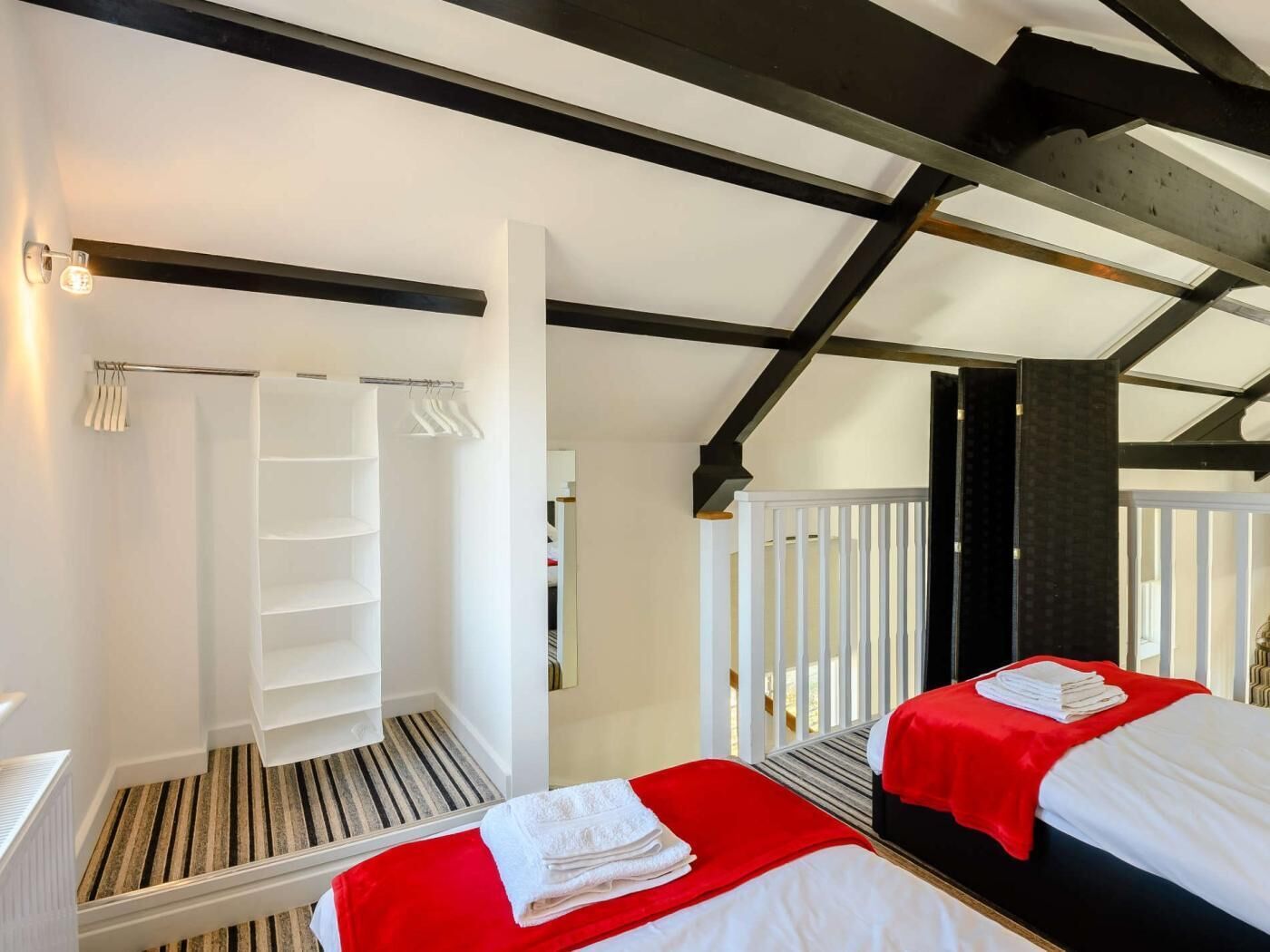 A room with two beds, a white wardrobe, a wooden ladder, and a white railing.
