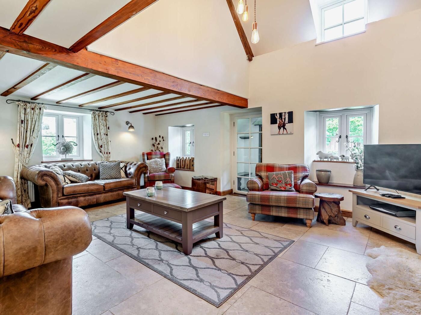A spacious living room with a high ceiling, exposed wooden beams, a fireplace, a television, and a large window.