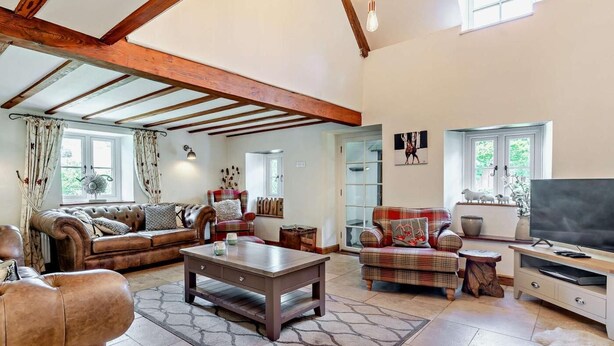 A spacious living room with a high ceiling, exposed wooden beams, a fireplace, a television, and a large window. - 3 Bed in Crickhowell (oc-56811) (Llangynidr)