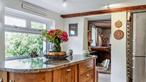 A kitchen with a wooden cabinet, a vase with flowers, and a view of the outdoors. - 3 Bed in Crickhowell (oc-56811) (Llangynidr)