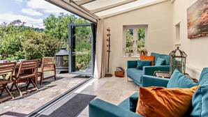 An open-plan living area with a glass door leading to an outdoor patio, a blue sofa, a small table, and a decorative lantern. - 3 Bed in Crickhowell (oc-56811) (Llangynidr)