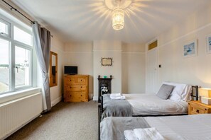 A bedroom with two beds, a dresser, a TV, a fireplace, and a window with curtains. - 3 Bed in Brixham (oc-56862) (Brixham)