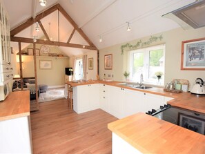 A kitchen with wooden beams, white cabinets, a central island, a stove, and a window with blinds. - 1 Bed in Dereham (oc-57021) (Mattishall)