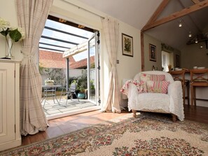 A cozy room with a white sofa, a patterned rug, and a view of a garden through a sliding glass door. - 1 Bed in Dereham (oc-57021) (Mattishall)