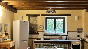 Una cocina con techo de madera, una ventana con celosía, un refrigerador y una mesa de comedor con sillas.
