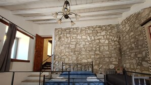 Un dormitorio con pared de piedra, cama con estructura de metal, puerta de madera y una escalera.