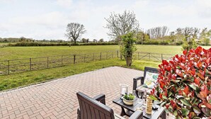 Eine Terrasse mit Sitzgelegenheit, Blick auf ein Wiesenfeld und ein Zaun.